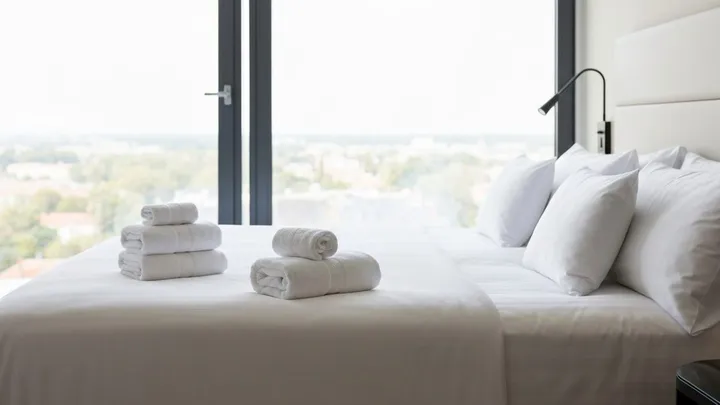 ผ้าเช็ดตัวพับเรียบวางบนเตียงขาวสะอาดพร้อมรับแขก Airbnb